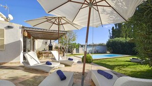 Eine Terrasse mit Lounge-Möbeln, einem Pool und einer Pergola mit Sonnenschirmen.
