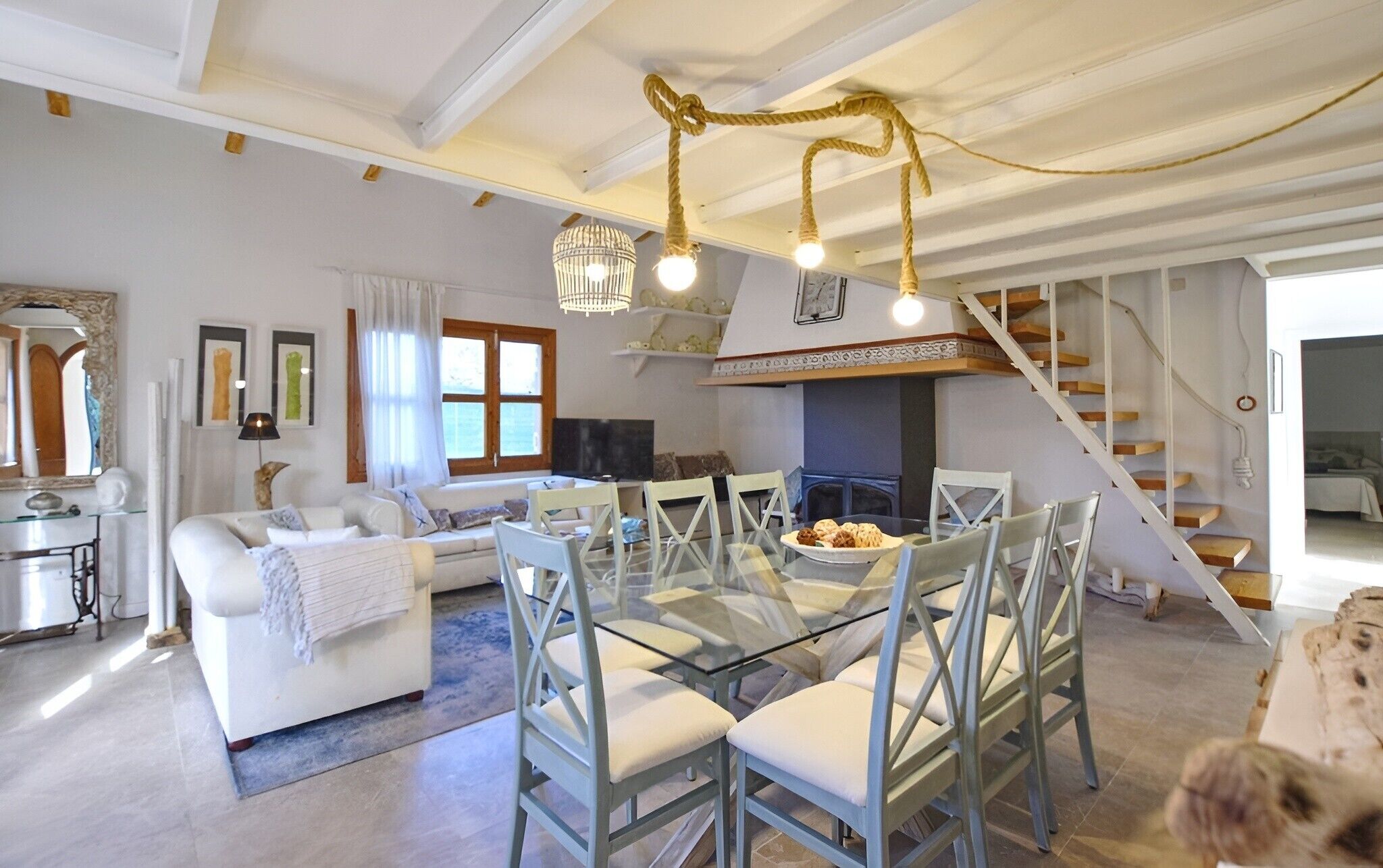 A spacious living area with a glass dining table, white sofas, and a staircase.