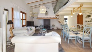 Ein geräumiger Wohnbereich mit Kamin, einem Esstisch mit Stühlen und einer Treppe, die in einen oberen Bereich führt.
