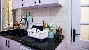 Une cuisine avec des armoires blanches, un plan de travail noir et un évier. On y trouve divers ustensiles de cuisine et un panier rempli de fleurs posé sur le plan de travail.