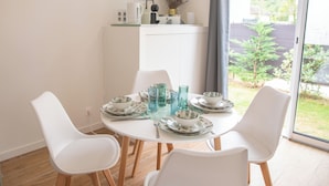Comedor con una mesa redonda para cuatro personas, sillas blancas y vista al exterior a través de un ventanal grande.