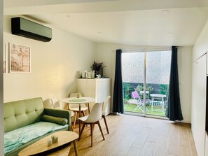 Ein modernes Wohnzimmer mit einem grünen Sofa, einem Esstisch mit Stühlen und einer Küchenzeile mit Geräten.