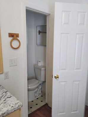 A bathroom with a toilet, a wooden toilet paper holder, a mirror, and a door. - Soothing 1-bedroom mobile home with AC in charming Buda (Buda)