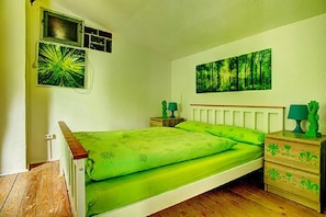 Una habitación con cama, mesita de noche, estante en la pared y un cuadro.