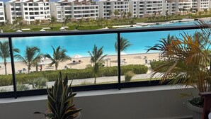 Ein Balkon mit Blick auf einen Strand, Palmen und einen Pool.