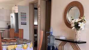 Ein Essbereich mit Tisch für zwei Personen, einem Stuhl mit blau-weißem Muster, einem Wasserspender und einem dekorativen Spiegel an der Wand.