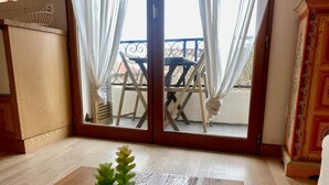 Une pièce dotée d’une porte-fenêtre coulissante donnant sur un balcon, d’une petite plante en pot posée sur le sol et d’un meuble en bois situé à gauche.