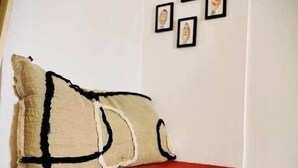 A bed with a red mattress and two pillows, a white wall with framed pictures, and a corner of a room with a white ceiling. - "Ribot" Coquet studio in the heart of Sète, Air conditioning & Wifi (Sète)