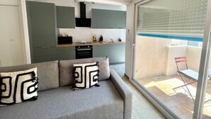 A modern apartment with a grey sofa, kitchen area, and a balcony with a red chair. - "Tango" T2 Air-conditioned, Town-centre, Parking, Wifi (Sète)