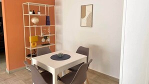 A dining area with a white table and four chairs, a white shelving unit with various items, and a framed picture on the wall. - "Tango" T2 Air-conditioned, Town-centre, Parking, Wifi (Sète)