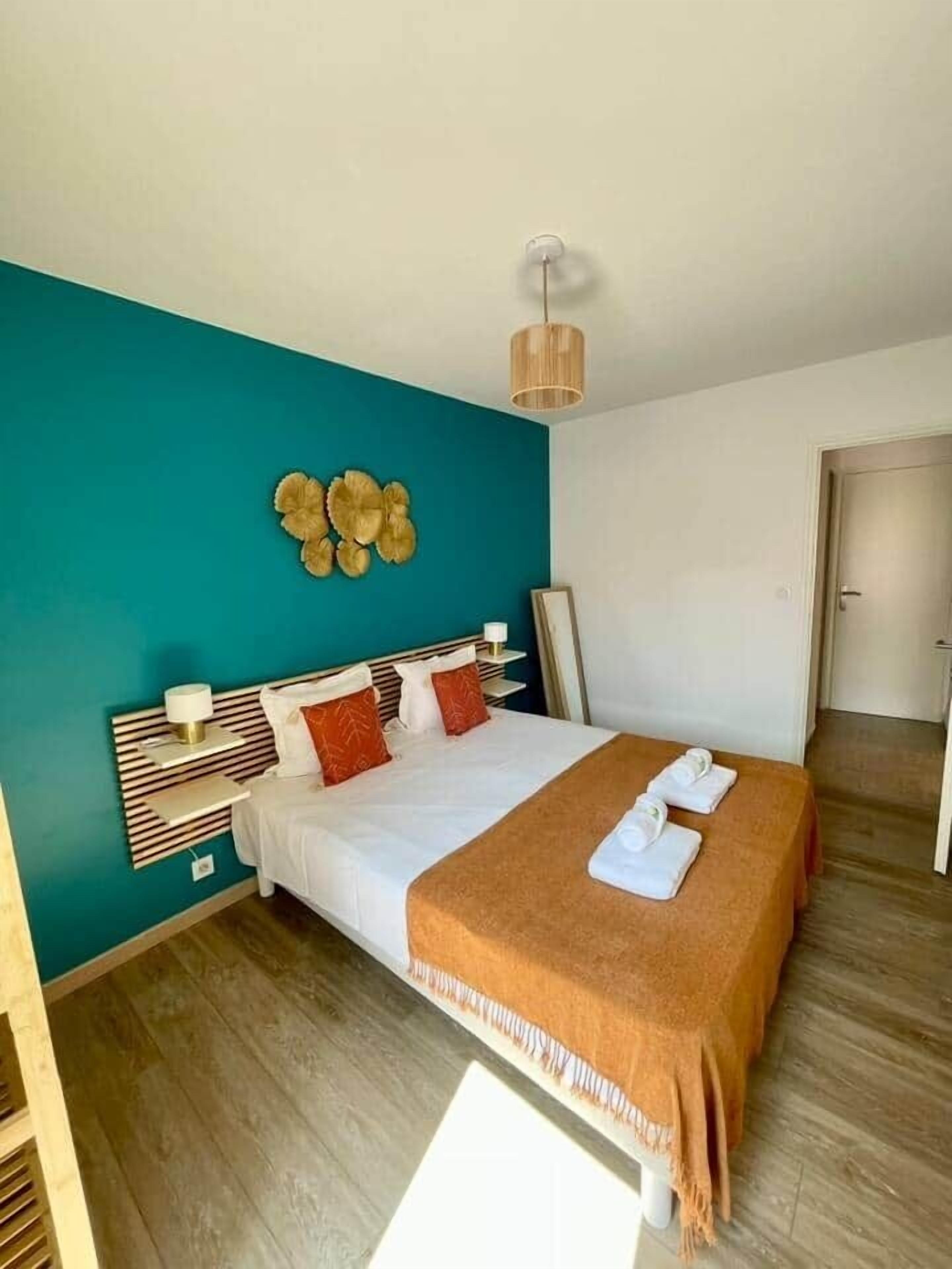 Une chambre d’hôtel avec un lit, une table de chevet, une lampe fixée au mur et une porte.