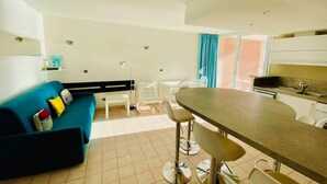 A modern kitchen with a bar area, a blue sofa, and a dining table with bar stools. - "578" Superb T2 Sea Front, Parking, Air Conditioning (Sète)