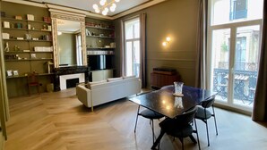 Amplia sala de estar con una mesa de comedor, un sofá y una chimenea. Se observan estanterías y un televisor al fondo.