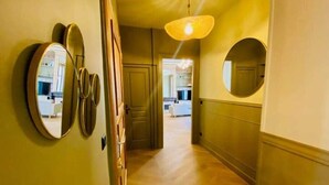 Un pasillo con piso de madera, un espejo redondo a la izquierda y una puerta que da a otra habitación.