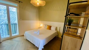 Habitación de hotel con cama, balcón, una lámpara colgante original y un mueble estante de madera.