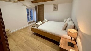 Un dormitorio con una cama de madera, una mesita de noche con una lámpara, una ventana con cortinas y un cuadro en la pared.