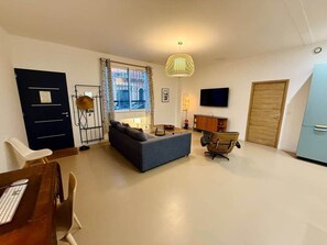 Un salon moderne avec un canapé, une table à manger et des chaises. Un téléviseur est fixé au mur, il y a une fenêtre avec des rideaux et une porte.