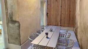 Un patio con una mesa larga y sillas, una cerca de madera y una pared con un respiradero.