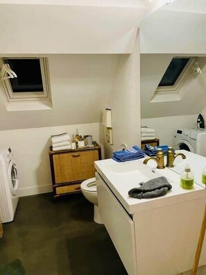 Une petite salle de bain comprenant des toilettes, un lave-linge, un lavabo avec un miroir et une fenêtre.