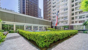 A paved courtyard with a neatly trimmed hedge, modern buildings in the background, and a flagpole with a flag. - Live Downtown 2BR Apartment W/ 2 TV near Downtown (Santiago)