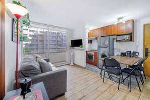 Eine kompakte Wohnung mit Küchenzeile, Essbereich, einer Couch und einem großen Fenster.