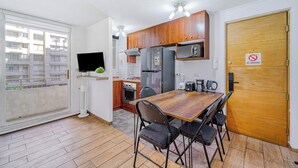 A compact kitchen with wooden cabinets, a refrigerator, a microwave, and a dining table with chairs. - Live Downtown 2BR Apartment W/ 2 TV near Downtown (Santiago)