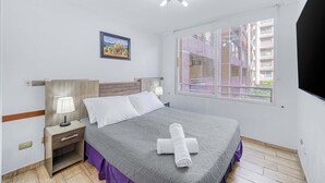 A neatly arranged bedroom with a bed, bedside tables, a lamp, and a window with a view of buildings. - Live Downtown 2BR Apartment W/ 2 TV near Downtown (Santiago)