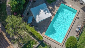 An aerial view of a rectangular swimming pool with a stone border, surrounded by a stone patio and lush greenery. - Podere Bagnoli farmhouse with swimming pool and sea view (Toscana)