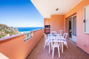 Ein Balkon mit Tisch und Stühlen, Blick auf das Meer, und ein Gebäude mit rosa Fassade.