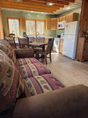 A cozy kitchen with wooden cabinets, a dining table with chairs, and a refrigerator.