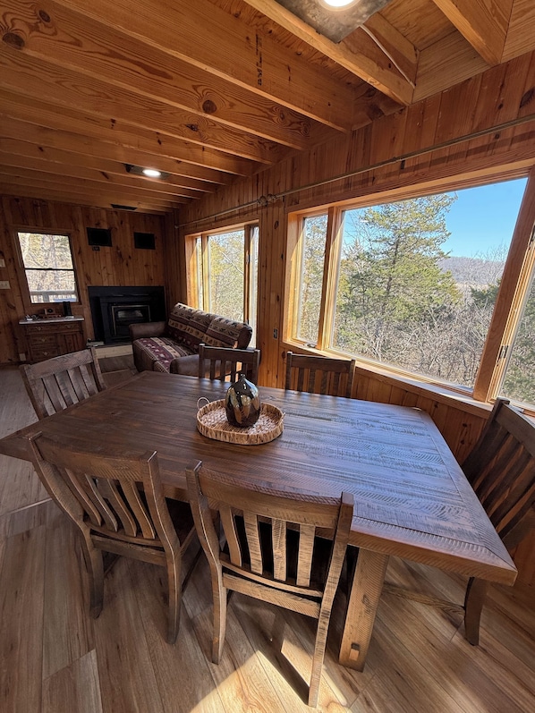 A wooden interior with a large dining table, chairs, and a fireplace.