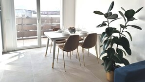 En matplats med ett bord för fyra personer, stolar, en krukväxt och utsikt genom en skjutdörr i glas till en balkong utomhus.