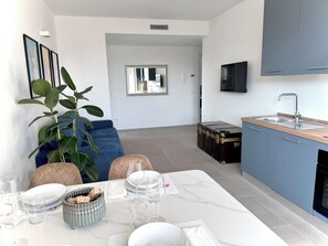 A modern kitchen with blue cabinets, a dining area with a table set for two, and a large potted plant. - Jungle Sarnico Color Suites  -Garage - Self check - 2 min from the lake and downtown (Sarnico)