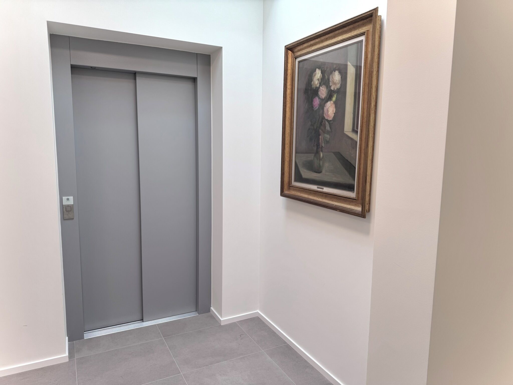 A hallway with a grey elevator and a framed painting on the wall.