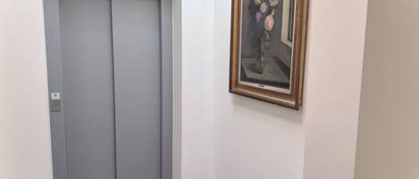 A hallway with a grey elevator and a framed painting on the wall.