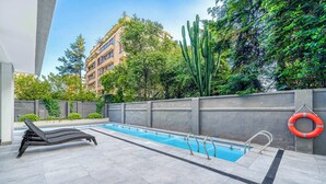 En swimmingpool med en solstol, en livboj och en betongvägg som är delvis täckt av grönska.