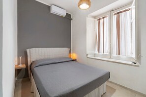 Une chambre à coucher comprenant un lit, une lampe de chevet, une fenêtre avec des rideaux et un appareil de climatisation.