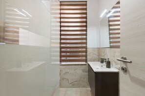 Une salle de bain moderne avec une douche à parois de verre, un lavabo en marbre et un grand miroir.