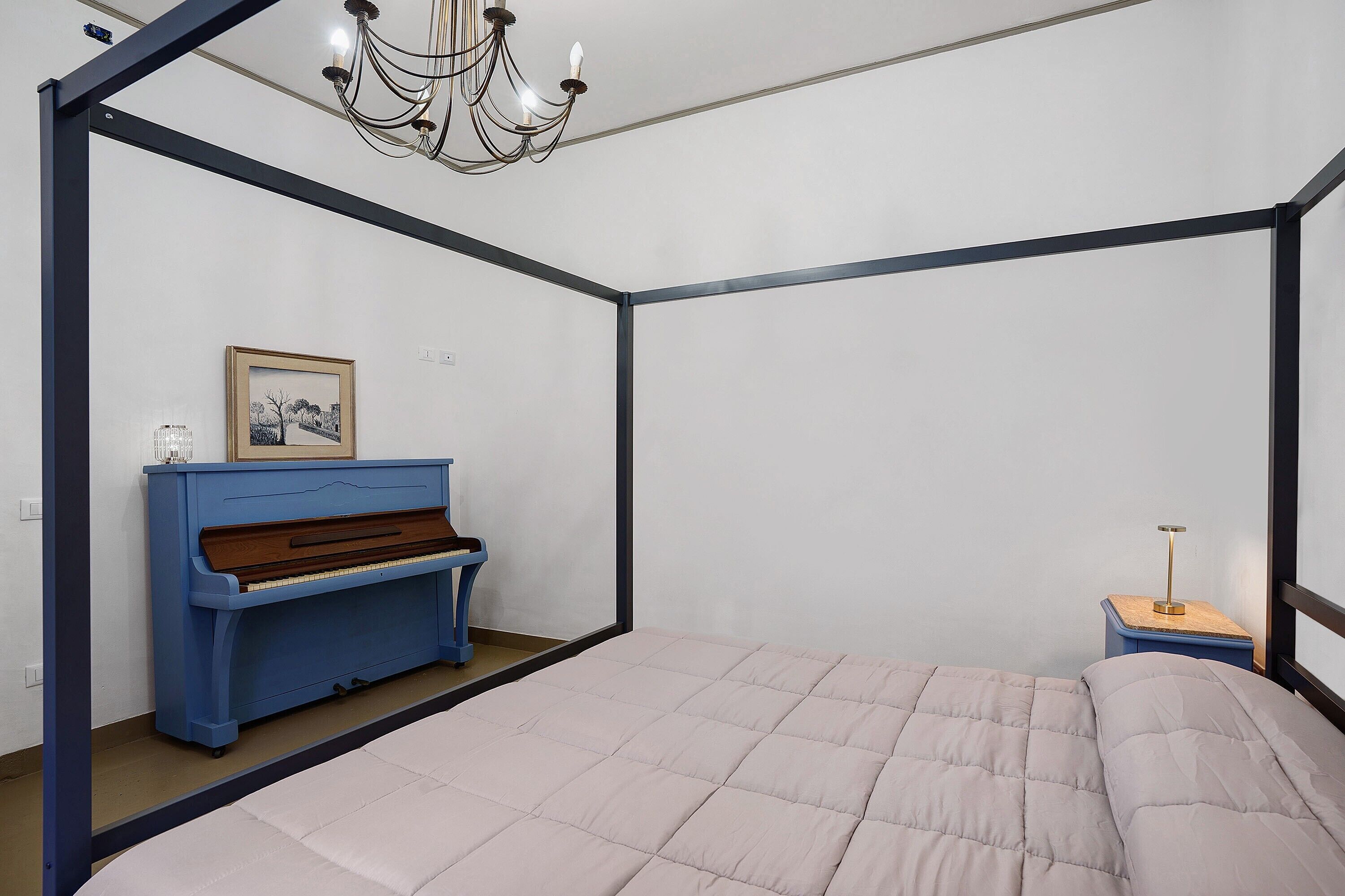 A bedroom with a bed, a piano, a nightstand, and a chandelier.