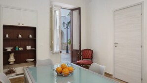 A dining area with a glass table, chairs, a red upholstered chair, a white cabinet, and a door. - Apartment 'Superior  Il Cortiletto 21' with Shared Terrace, Wi-Fi and Air Conditioning (Marsala)