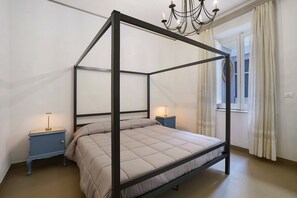 Un lit à baldaquin avec une tête de lit, deux tables de chevet, un lustre et une fenêtre avec des rideaux.