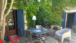 Eine Außenpatio mit Tisch und Stühlen, umgeben von viel Grün und einem Steinboden.