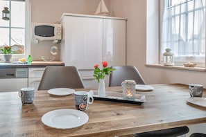 A dining area with a wooden table set for four, a white cabinet, a microwave, and a window with a view.