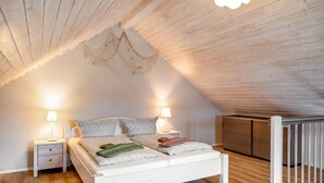 Une chambre avec un plafond en pente, un lit avec des oreillers, deux lampes de chevet, une table de chevet et un plancher en bois.