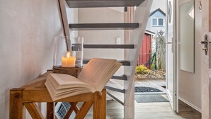 Un banc en bois avec un livre et une bougie, un verre d’eau, et un escalier menant à une porte.