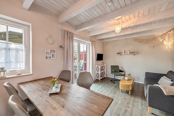 A room with a wooden dining table, chairs, a sofa, a TV, and a small side table.