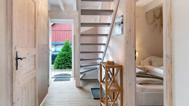 A hallway with a wooden door, a staircase, a small table with a candle, and a bed with a patterned pillow. - Swedish House Zierow - Baltic Sea - House 23b (Zierow)