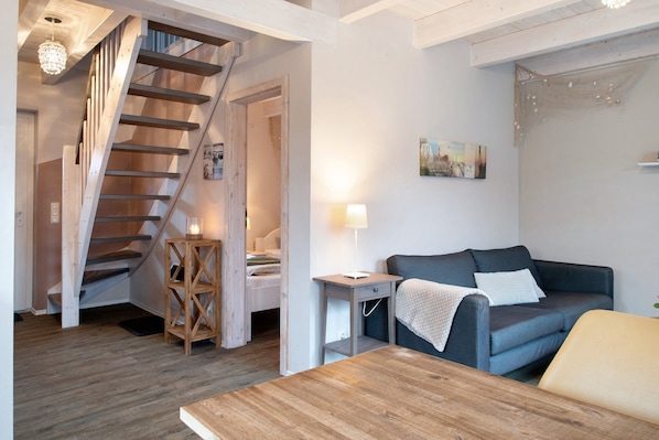 A room with a wooden staircase, a sofa, a small table, and a lamp.