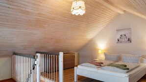 A bedroom with a sloped ceiling, a bed with patterned pillows, a wall-mounted lamp, and a painting. - Swedish House Zierow - Baltic Sea - House 23b (Zierow)