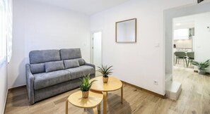 A modern living room with a grey sofa, two small round tables with potted plants, and a kitchen visible through an open doorway. - Bright Modern Home with Terrace (Madrid)